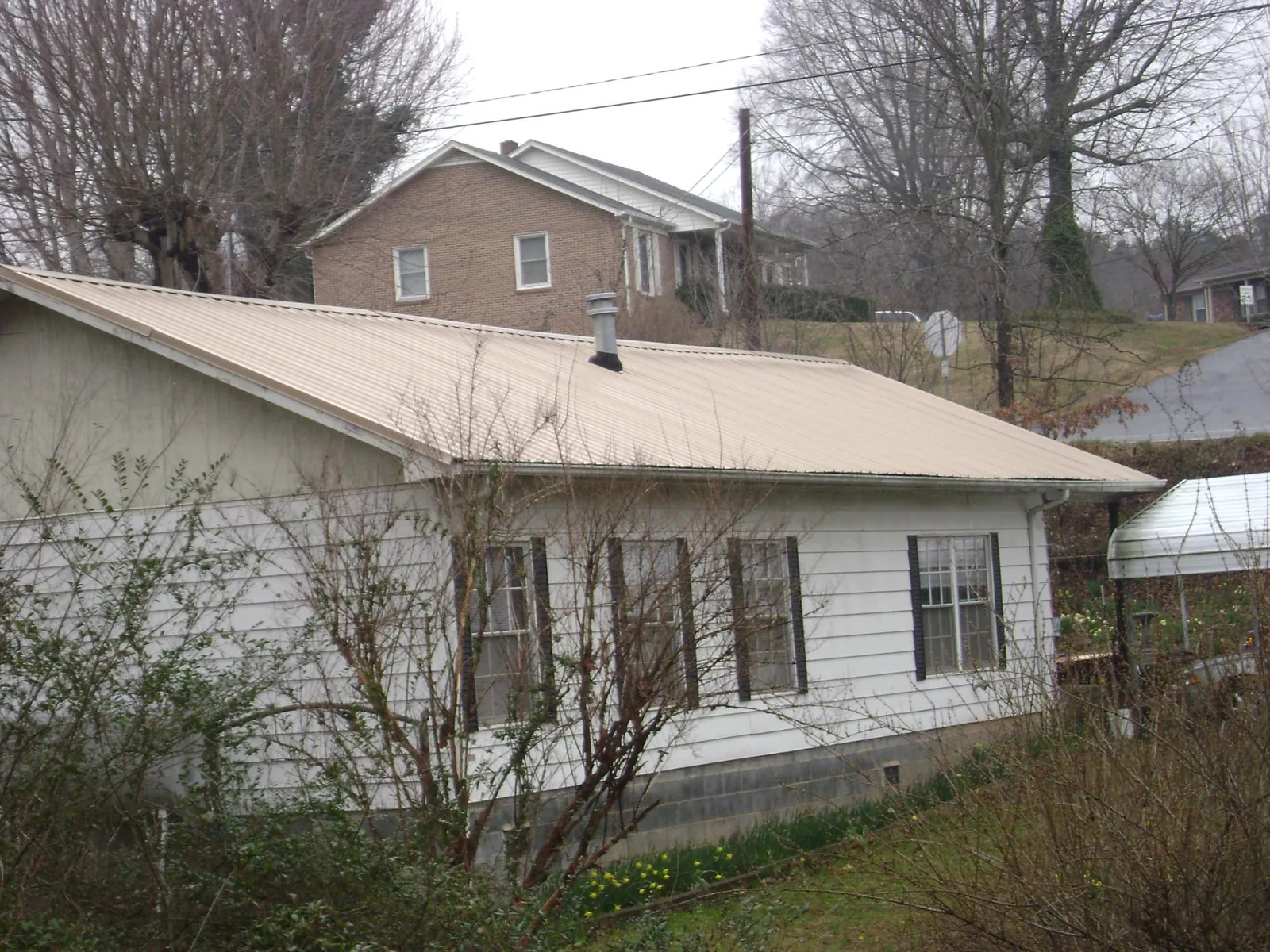 Tan metal roof on a white sided house set into a hillside — Commercial Roofing by Roofing Brothers in Suquamish